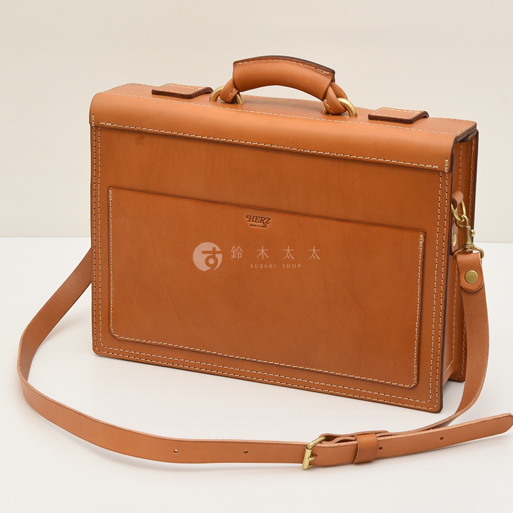 職人手作皮革兩用機師箱，呈現自然棕色，皮革質地，配有頂部提把、金屬扣環及可拆卸肩帶。箱體正面有平整的口袋和細緻的縫線。