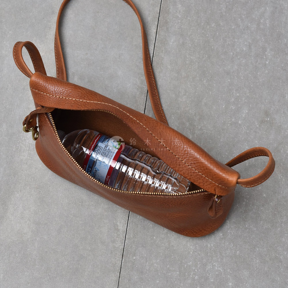 皮革斜背包內有一瓶透明塑膠瓶裝水，背包開口拉鍊拉開，露出部分瓶身，背包為棕色皮革材質，背帶為細長皮革。