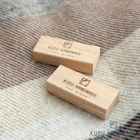 兩塊淺色天然木質長方形香楠木條，表面印有黑色「KUSU HANDMADE ECO BLOCK」字樣與品牌標誌，平置於紋理織物背景上。