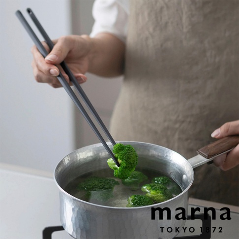 marna 品牌有矽膠長筷，這雙筷子是 31 公分的。圖中，一雙灰色的長筷正夾著一塊綠色的花椰菜，準備放入一鍋熱水中。