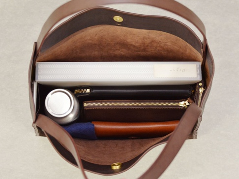 職人手作皮革Organ方形托特包，M尺寸，深棕色皮革，內部展示：一個文件夾、一個銀色保溫杯、一個黑色皮夾、一個棕色零錢包和一個藍色織物。