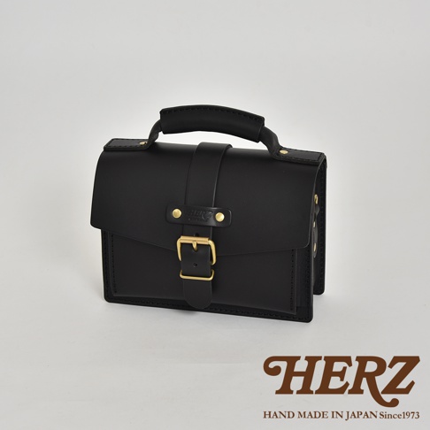 職人手作黑色皮革迷你單肩包，配有金色金屬釦環、兩顆鉚釘及品牌標誌，上方有提把。