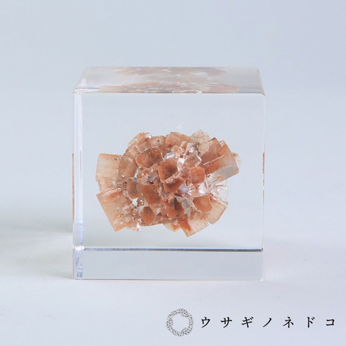 透明立方體內嵌有簇狀的霰石礦石，呈現出粉褐色與淺橘色調，礦石表面有許多細小的晶體結構。