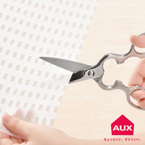 一隻手持銀色不鏽鋼剪刀，正在剪裁印有淺棕色條紋圖案的白色防汙紙。