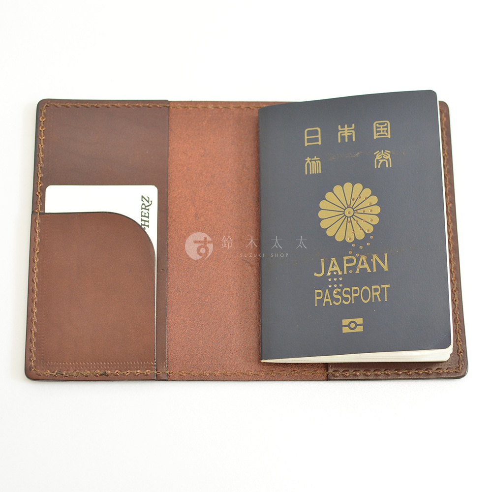 職人手作皮革護照套，深棕色牛皮材質，內有信用卡槽，右側置入一本深藍色封面、印有金色日本國徽、JAPAN PASSPORT字樣的護照。