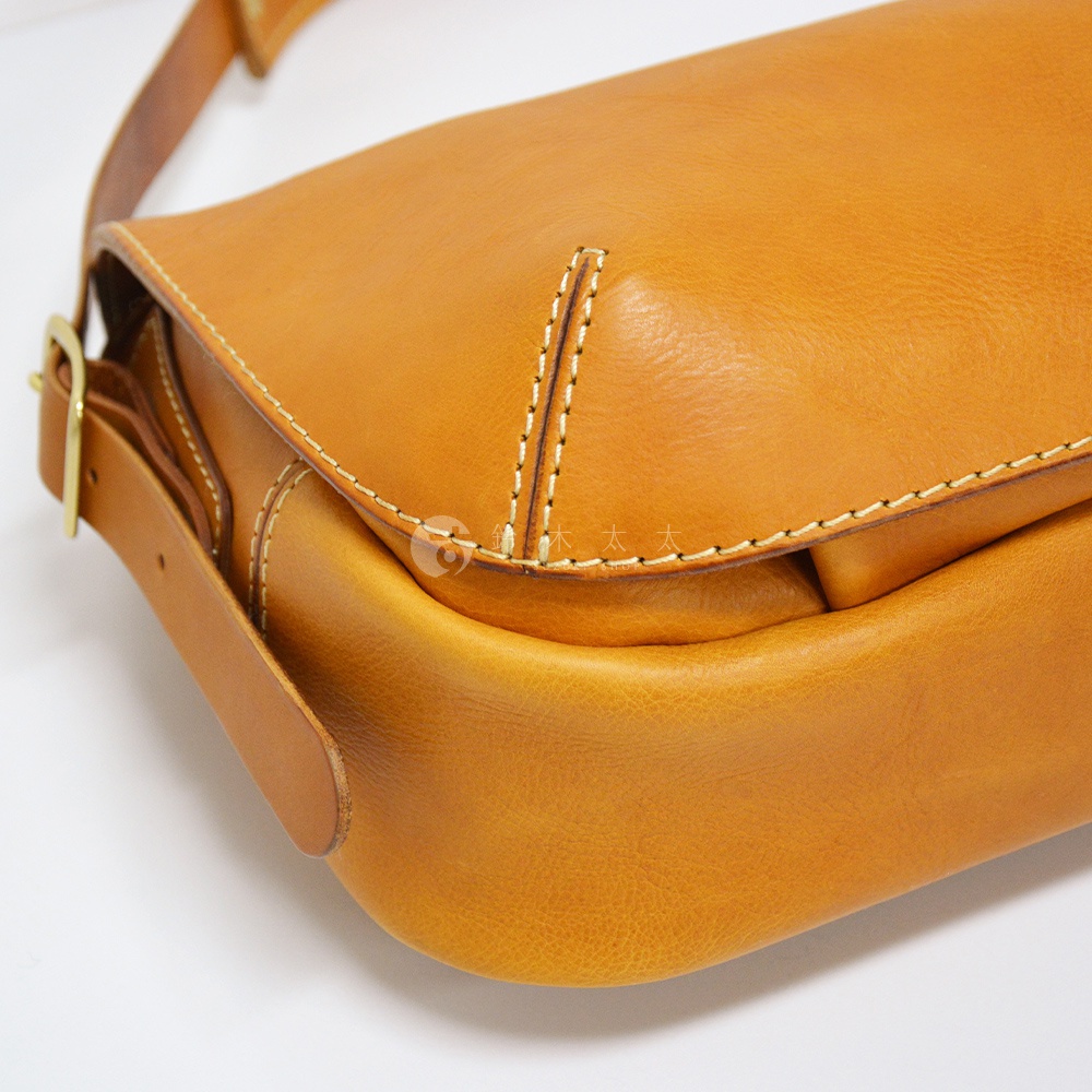焦糖色皮革復古翻蓋郵差包，細緻縫線，搭配黃銅色金屬扣環，展現職人手作質感。