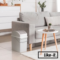 一個白色矮版垃圾桶，配有灰色搖蓋，側面有一個金屬提把，置於客廳地毯上，旁邊是沙發和茶几。