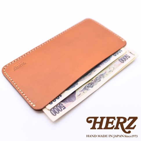 日本HERZ品牌職人手作皮革紙鈔夾，選用溫潤的淺棕色皮革製成，表面帶有細緻的壓印Logo，設計簡約輕薄，底部露出夾層中收納的日圓紙鈔，呈現手工縫線細節與皮革質感，整體風格洗鍊且極具日式工藝美感。