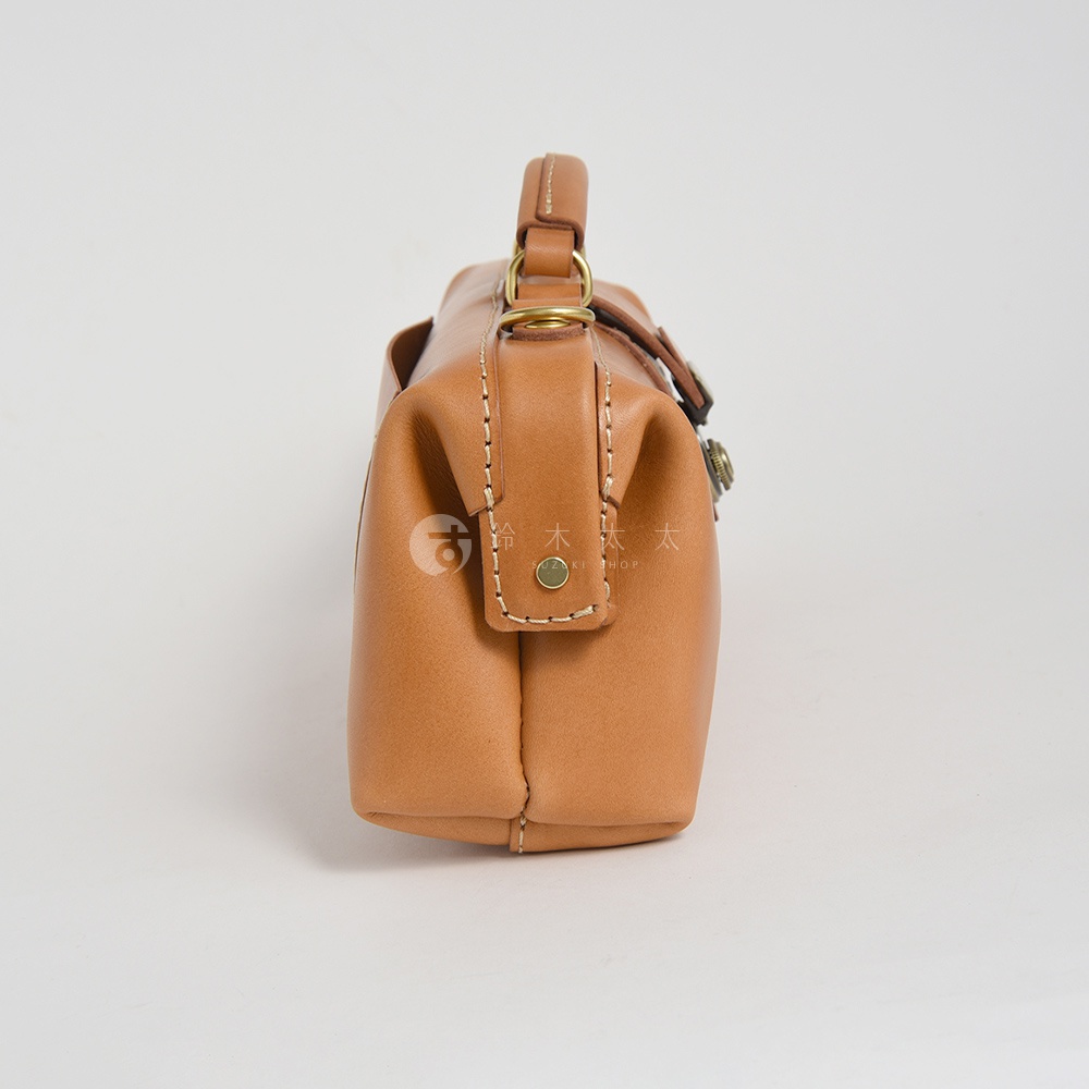 以日式職人手作為特色，此款HERZ橫長形杜勒斯皮革側背包，以日文標記「鈴木 太太」及英文「UZAKI SHOP」字樣，展現精緻工藝，以淺棕色皮革製成，從側面角度捕捉其經典設計。