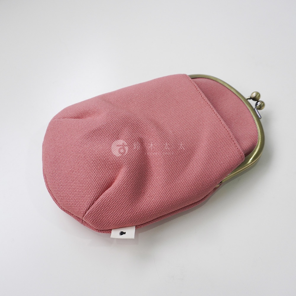 一個粉紅色的帆布腰掛口金包，帶有黃銅色的開合處，包包上印有淺色的圖案和一個小魚形狀的標籤。