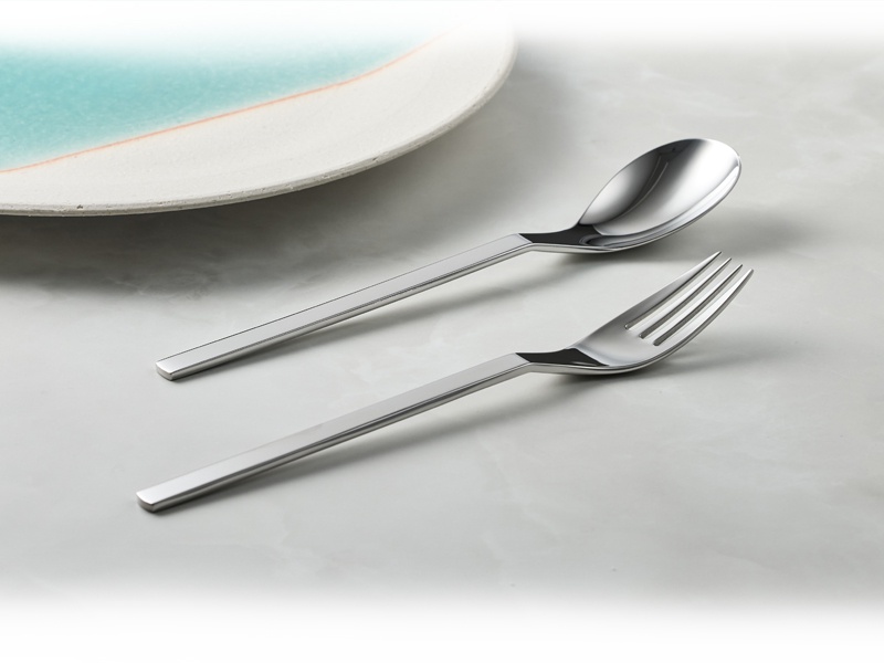 一個不鏽鋼叉子和一把湯匙，靠近一個有藍色邊緣的白色盤子。