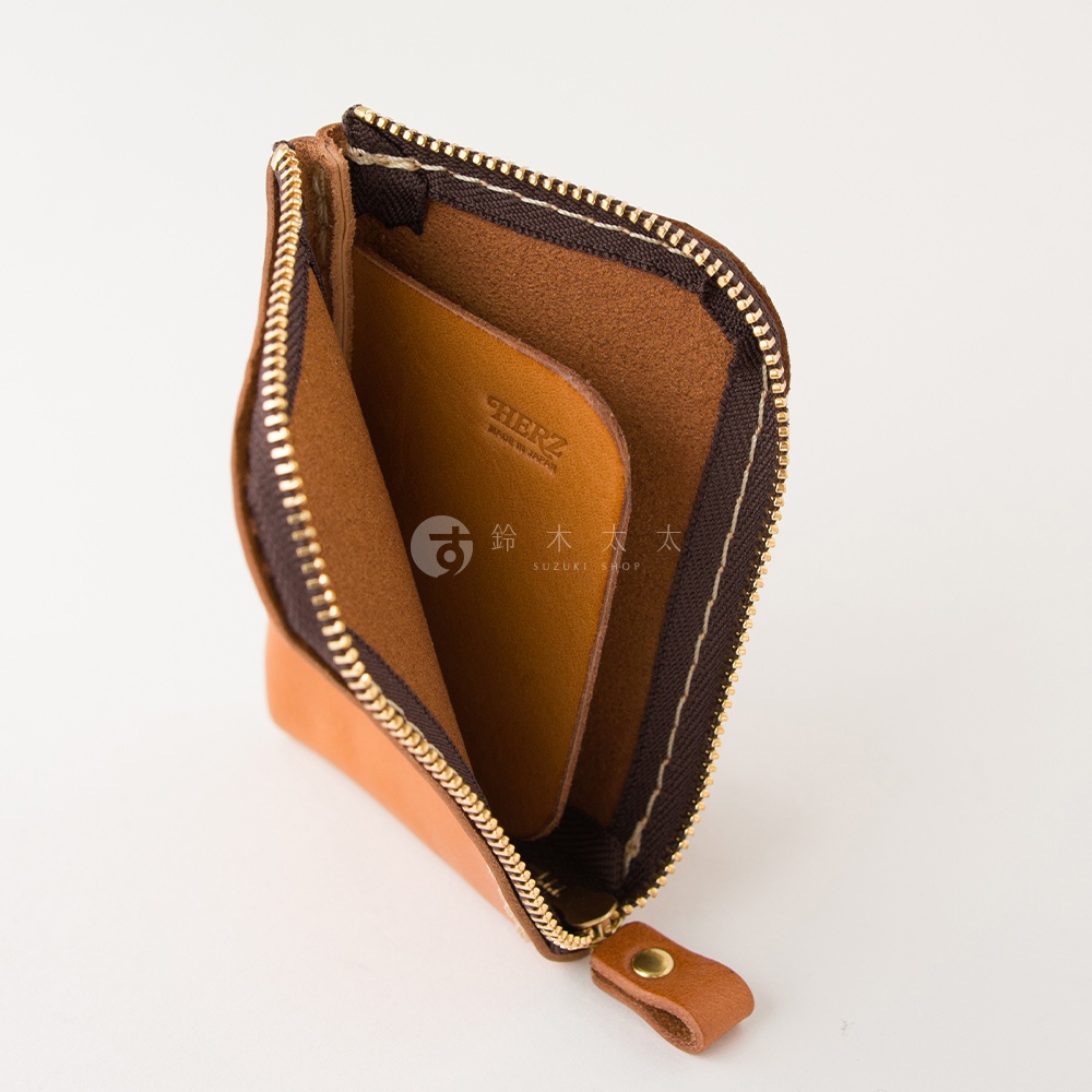 一個日本HERZ職人手作的棕色皮革迷你錢包，錢包採L型拉鍊設計，打開後可見內部有一個皮質分隔層，袋內燙印有品牌標誌與日本製造的字樣，表面呈現溫潤的皮革質感。
