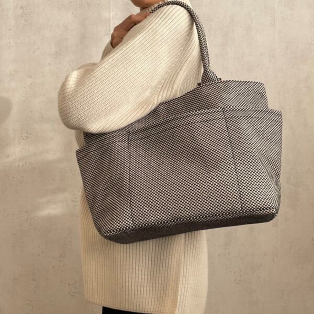 模特兒身著米白色毛衣，肩背一款深灰色與白色格紋刺子織手提托特包，包款為 L 尺寸，具有明顯的格紋紋理和外部口袋。