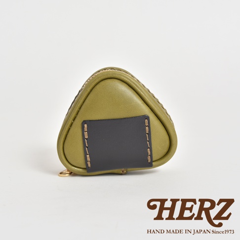 橄欖綠皮革製成的三角飯糰造型小物收納包，正面有黑色皮革裝飾片，以明顯的縫線固定。