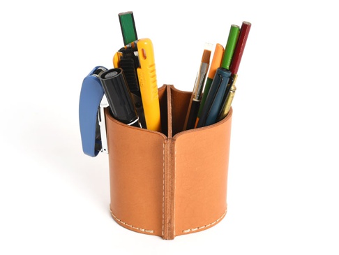 棕色皮革筆筒，有兩個隔間，內含一支藍色釘書機、一支黑色麥克筆、一支黃色美工刀、一支綠色鉛筆、一支畫筆、一支橘色筆、一支藍色鋼筆和一支紅色筆。