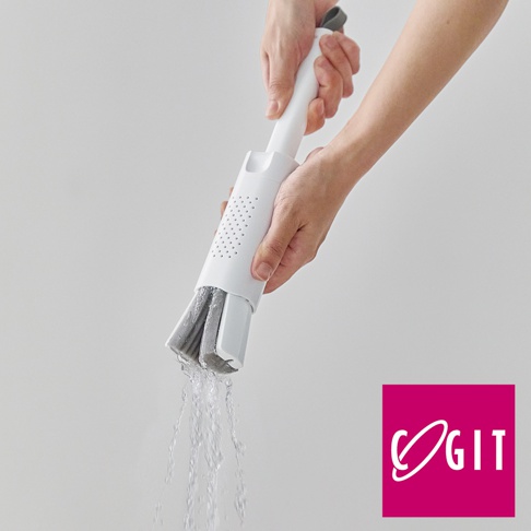 一隻手握著白色塑膠手柄的推拉式海綿刷，刷頭由灰色海綿製成，下方有水流出。