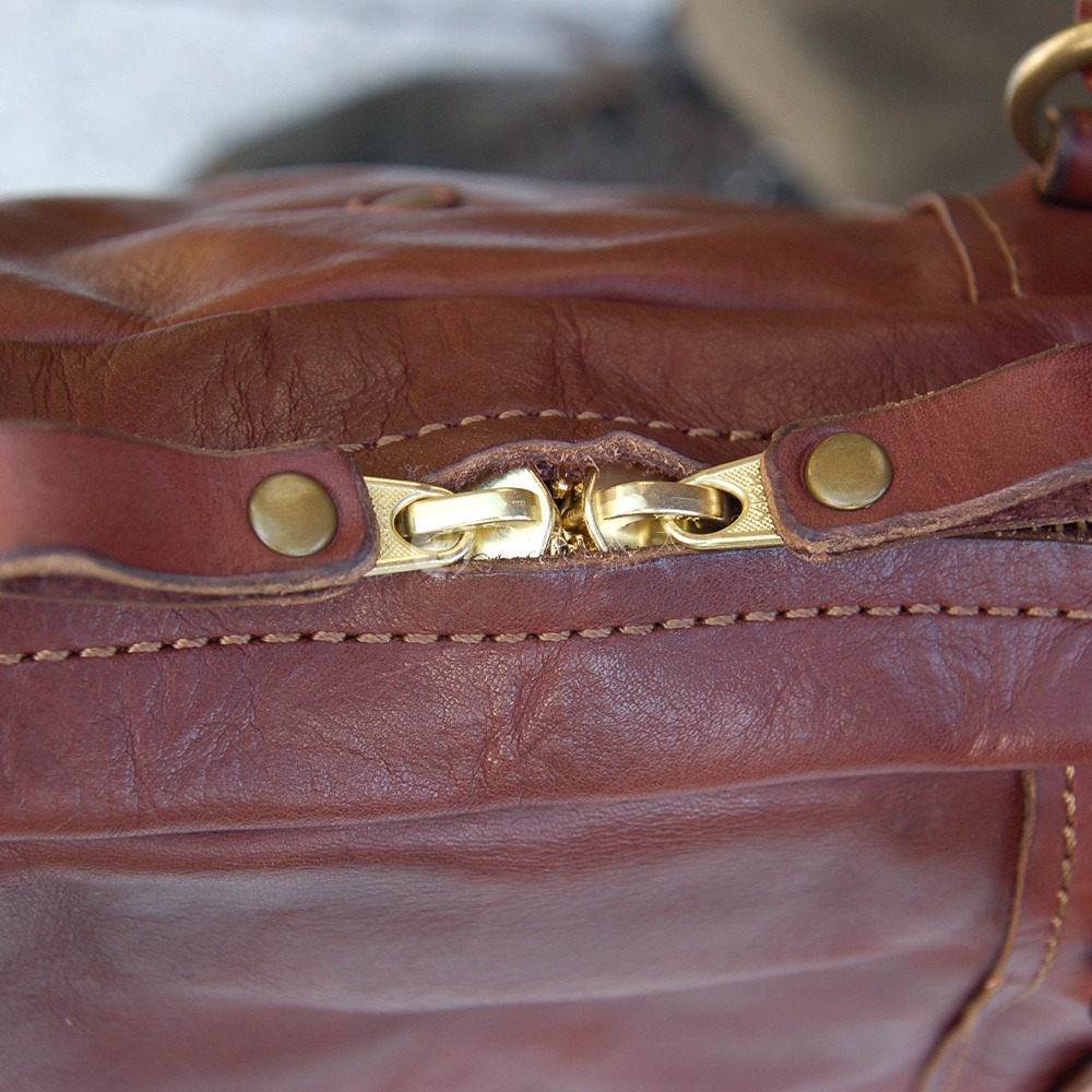 職人手作皮革迷你波士頓包，深棕色水洗皮革，特寫頂部金色拉鍊與兩側皮革壓扣。