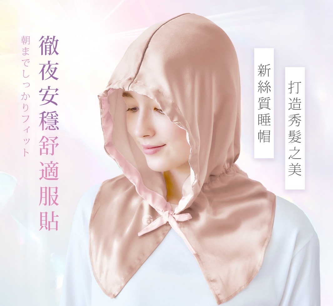 一位女性戴著一頂淺粉色絲質柔亮美髮晚安睡帽，睡帽為連帽設計，邊緣有抽繩，領口處有一個蝴蝶結裝飾。