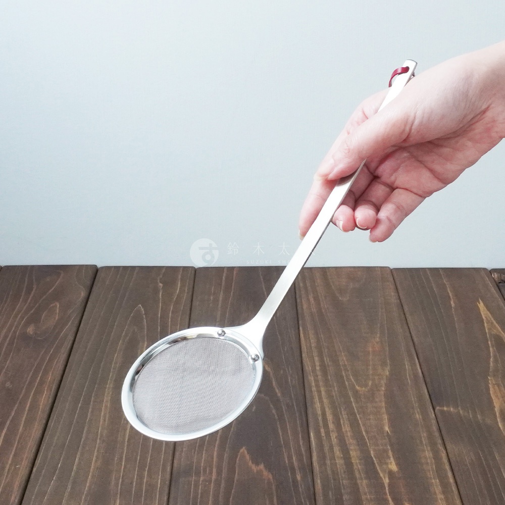 一只手正握著一把不鏽鋼萬用撈泡勺，勺頭為橢圓形，內部有細密的網篩，勺柄末端有紅色裝飾。