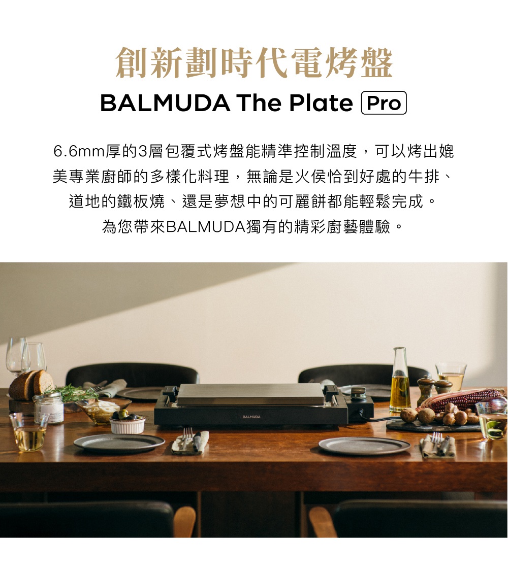 黑色 BALMUDA The Plate Pro 極致電烤盤，置於木質餐桌上，烤盤表面平坦，材質為金屬，周圍擺放著餐具、麵包、蔬菜和調味料，營造出用餐情境。