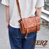 職人手作皮革水洗加工復古郵差包，採用棕色皮革製成，配有可調節肩帶和金屬扣環，整體呈現簡約復古風格。