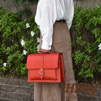 紅色皮革三用單扣商務後背包，帶有金屬扣環和縫線細節，由皮革製成。