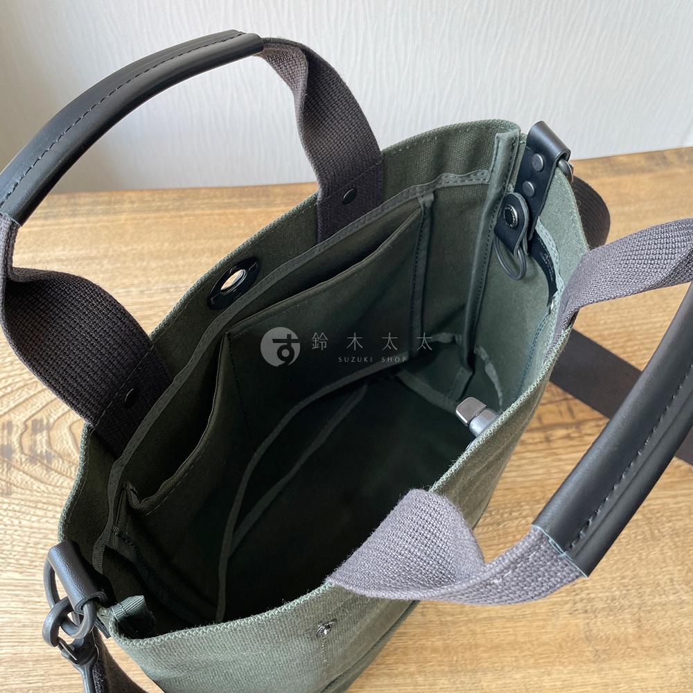 橄欖綠帆布材質的兩用托特包，內有多個隔層，搭配黑色皮革提把與織帶。