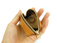 手持的職人手作皮革貝殼造型零錢包，顏色為自然焦糖色，材質為真皮。拉鍊為金色，內部可見兩個戒指。