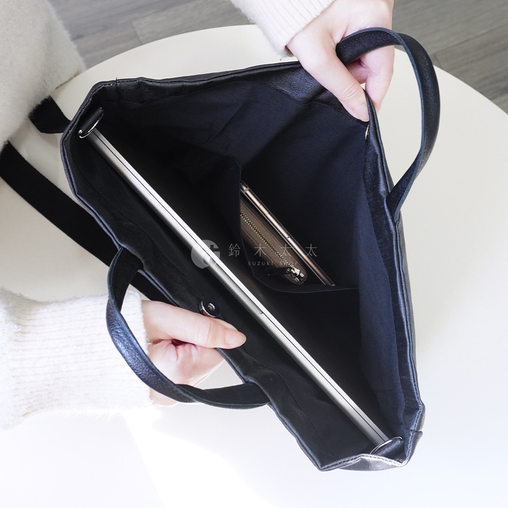 一位女士正將筆記型電腦放入黑色托特包中，包內還有一個手機零錢包。