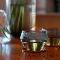 LAGOM 清透復古圓潤玻璃杯，S 尺寸，透明玻璃杯身，底部帶有金色金屬材質，杯壁凝結水珠，盛有淺黃色液體，置於木質桌面。