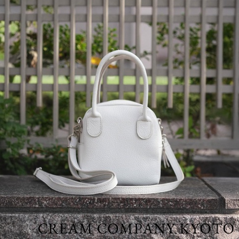 白色皮革手提包，附有可拆卸肩帶，包身呈貝殼狀，帶有雙提把和金屬配件。