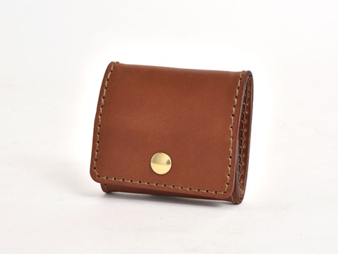 棕色皮革製作的箱型零錢包，帶有金色金屬按鈕，邊緣以米色縫線手工縫製。