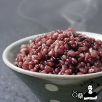 一碗裝滿深紅色十六穀米的陶瓷碗，米飯表面冒著輕煙，碗身有綠色和白色圓點圖案。