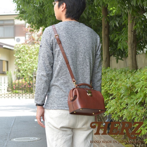 棕色皮革手作迷你醫生包，配有可調節的肩帶、頂部提把和金色金屬鎖扣，包身底部有四個金色金屬腳釘。