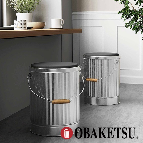 OBAKETSU 品牌標誌旁有兩個銀色金屬儲物桶凳子，皆有木製提把和黑色坐墊。