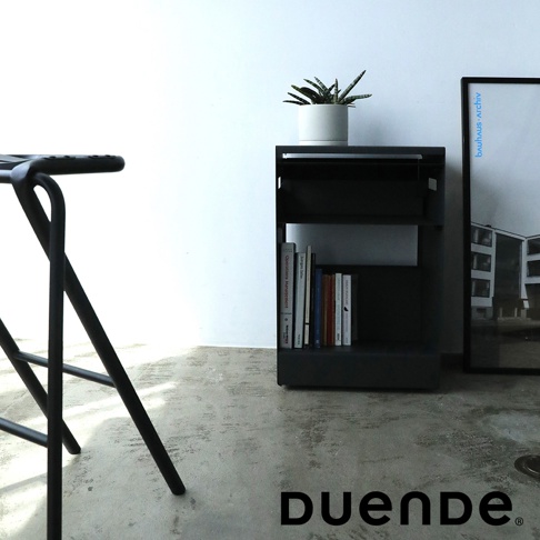 DUENDE 黑色收納推車，側面有書籍和盆栽，右側有 Bauhaus archiv 海報