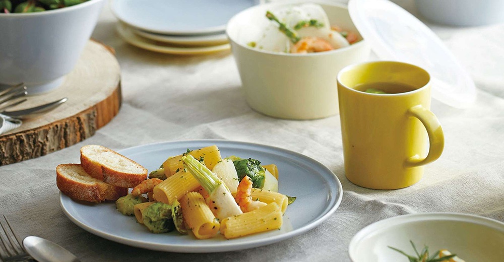 淺藍色盤子盛著義大利麵、蝦仁與蔬菜，旁邊是切片麵包、黃色馬克杯與淺黃色保鮮碗。