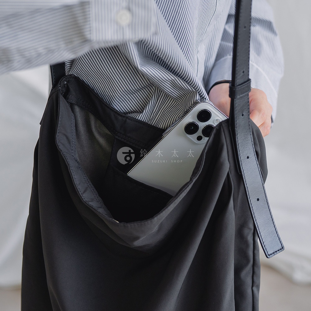 斜條紋襯衫的左側，一個黑色托特包的內袋裡露出了一部手機，包袋內側有一個印有「す 鈴木SUZUKI SHOP」字樣的黑色標籤。