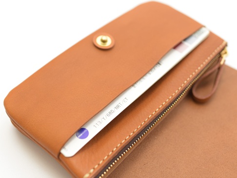 一件棕色皮革長夾，有金色按扣和拉鍊，可容納護照和機票。