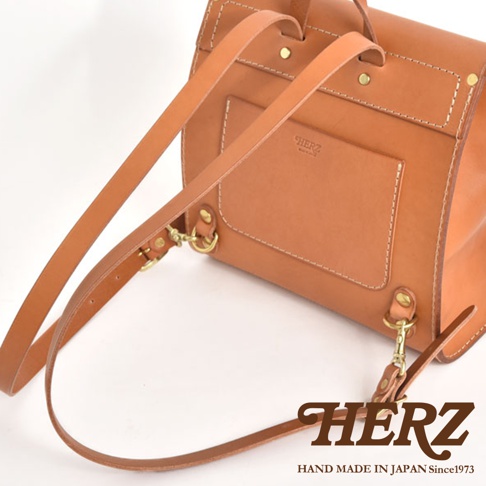 棕色皮革迷你後背包，翻蓋設計，附可調式肩帶和金色金屬扣環。包身有精緻的縫線細節，並印有品牌標誌。