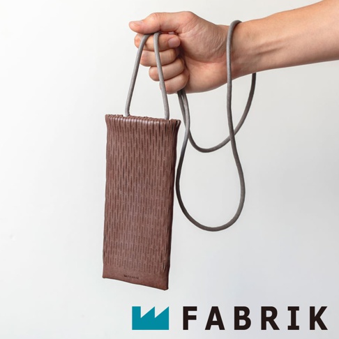 FABRIK 品牌皮革手機包，由皮革製成，帶有細長的條紋紋理，由手中掛著一條灰色的細繩。