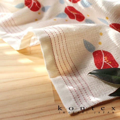 白色長毛巾，印有紅色山茶花圖案，搭配藍色水滴和黃色圓點。毛巾邊緣有紅色縫線裝飾，材質輕薄透氣。