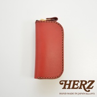 HERZ 品牌標誌，下方有 HAND MADE IN JAPAN Since1973 字樣，圖片主體為紅色皮革製的橢圓形拉鍊鑰匙包，有四鉤，採用手工縫線。