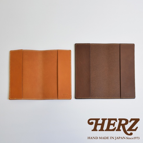 兩款日本HERZ職人手作皮革書套並排平放，左側為淺棕色皮革，右側為深棕色皮革，兩者皆為厚實耐用的手工質感，右下角印有品牌名稱，整體背景為純白風格。