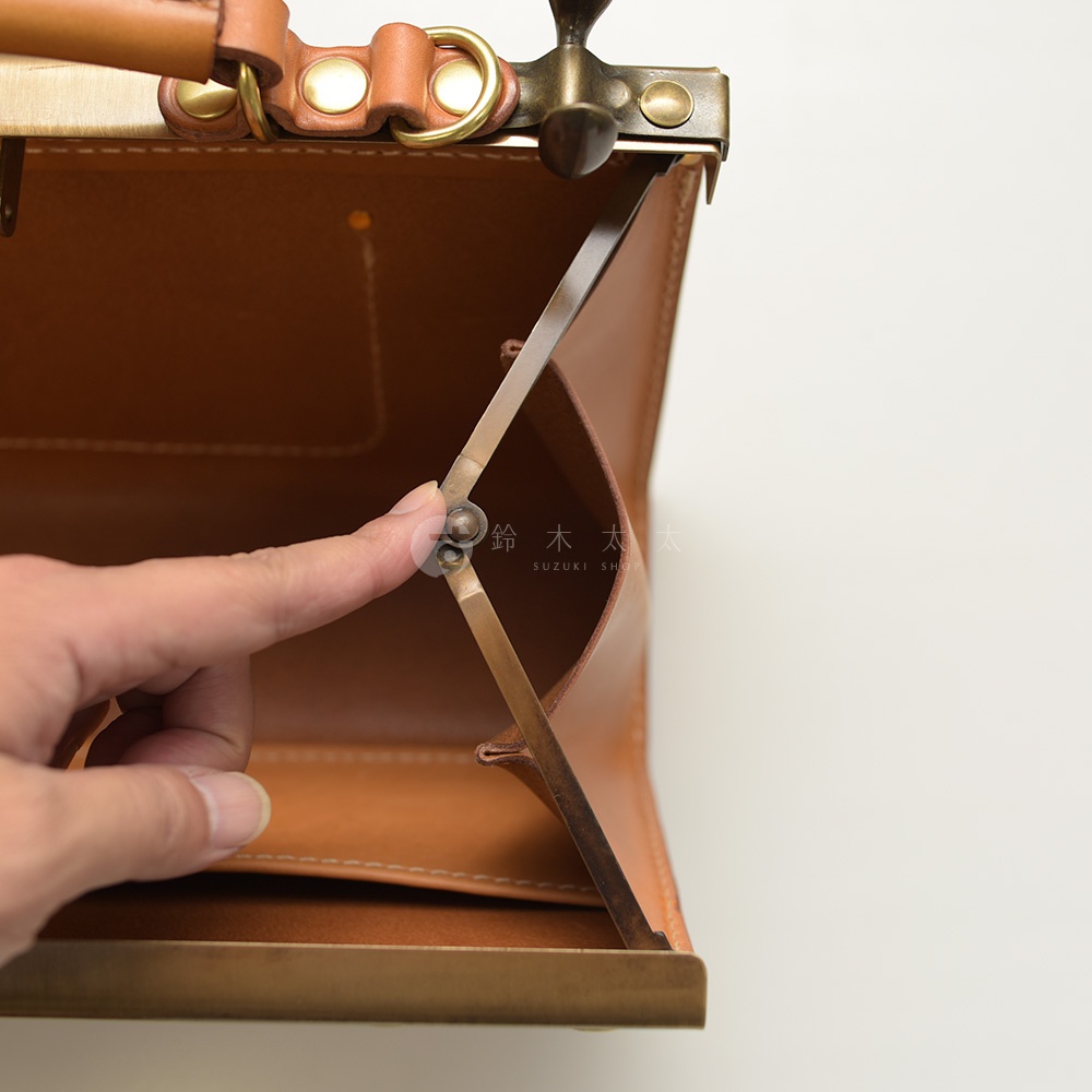 手被用於打開一個棕褐色皮革口金包，展示了其內部結構和黃銅金屬配件。