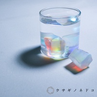 玻璃杯中盛有透明液體，杯內及杯外各有一塊不規則的稜鏡石，呈現虹彩色澤，主要為粉紅、黃、藍、紫等光影變化。