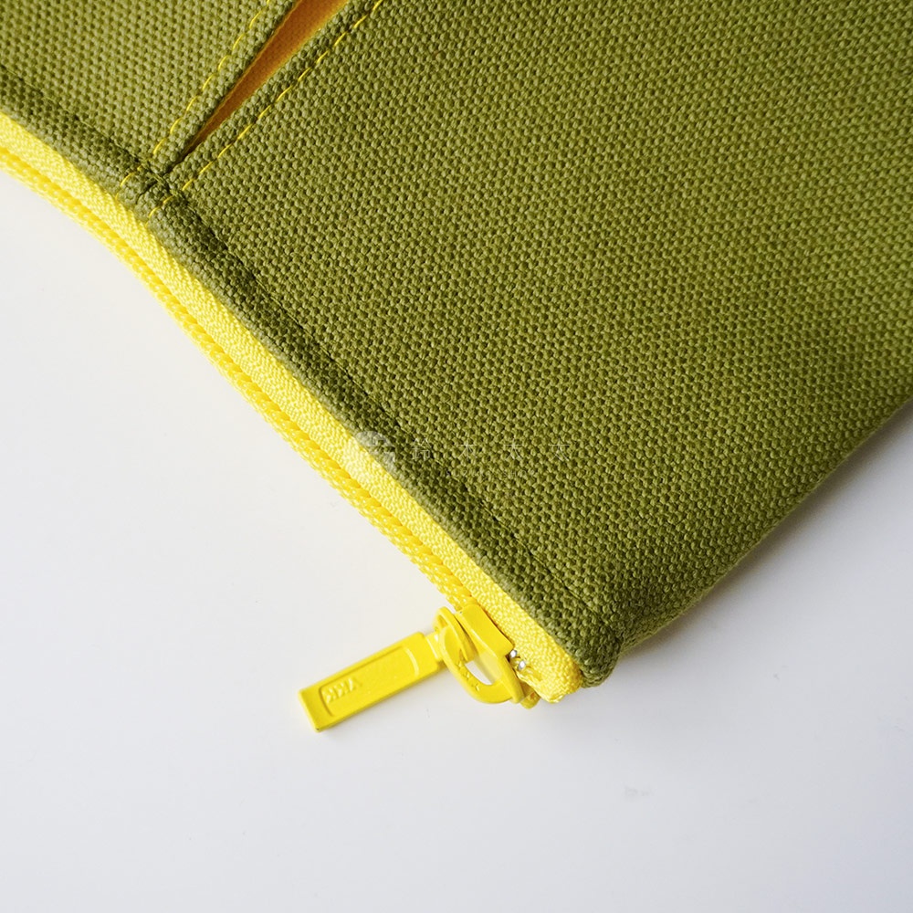 近距離拍攝京都KOSHO ougi系列帆布化妝收納包的角落，呈現橄欖綠色帆布材質的細緻紋理，搭配鮮黃色拉鍊與刻有YKK字樣的黃色金屬拉鍊頭，展現高品質的細節工藝。