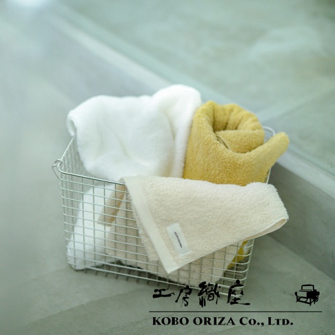 金屬籃中擺放著三條超細纖維毛巾，分別為白色、芥末黃色和淺米色。淺米色毛巾置於最前方，其左上方有品牌標籤。