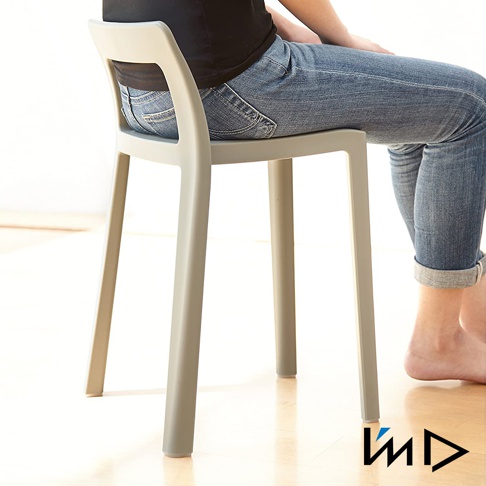 一個淺灰色一體成型塑膠短背椅凳，有四個椅腳，椅背有鏤空設計，一位身穿牛仔褲的人坐於其上。