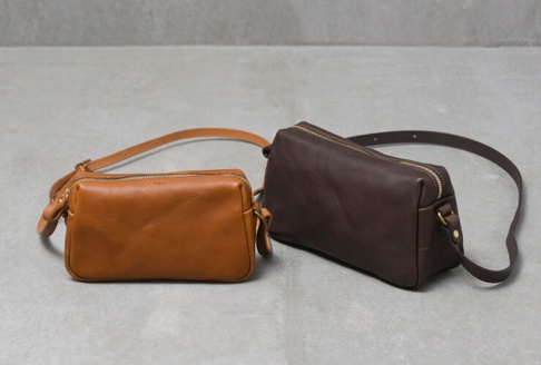 兩款職人手作皮革Organ輕巧拉鍊單肩包，一款為棕色皮革，另一款為深棕色皮革，均配有金色拉鍊和可調節皮革肩帶。